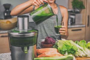woman pouring homemade green juice with a juicer and vegetables on the counter