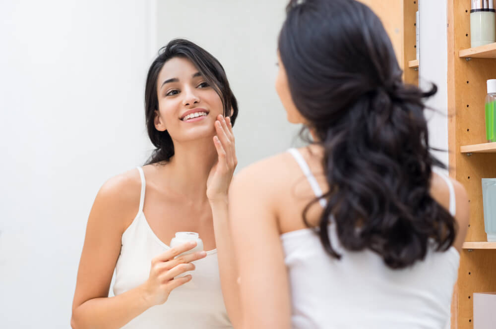 young woman in the bathroom admiring her reflection as she applies facial cream