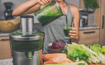 woman pouring homemade green juice with a juicer and vegetables on the counter