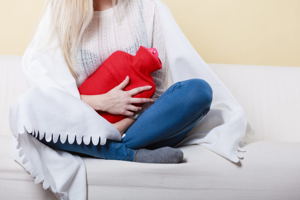 Woman holding a hot-water bottle to her stomach due to cramping